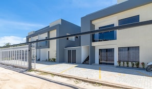 Un immeuble résidentiel moderne à plusieurs étages, doté d’un toit plat, de grandes fenêtres et d’un espace extérieur couvert agrémenté d’une clôture en métal.