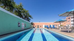 Una piscina con baldosas azules cristalinas, un muro verde y un edificio de fachada color melocotón al fondo.