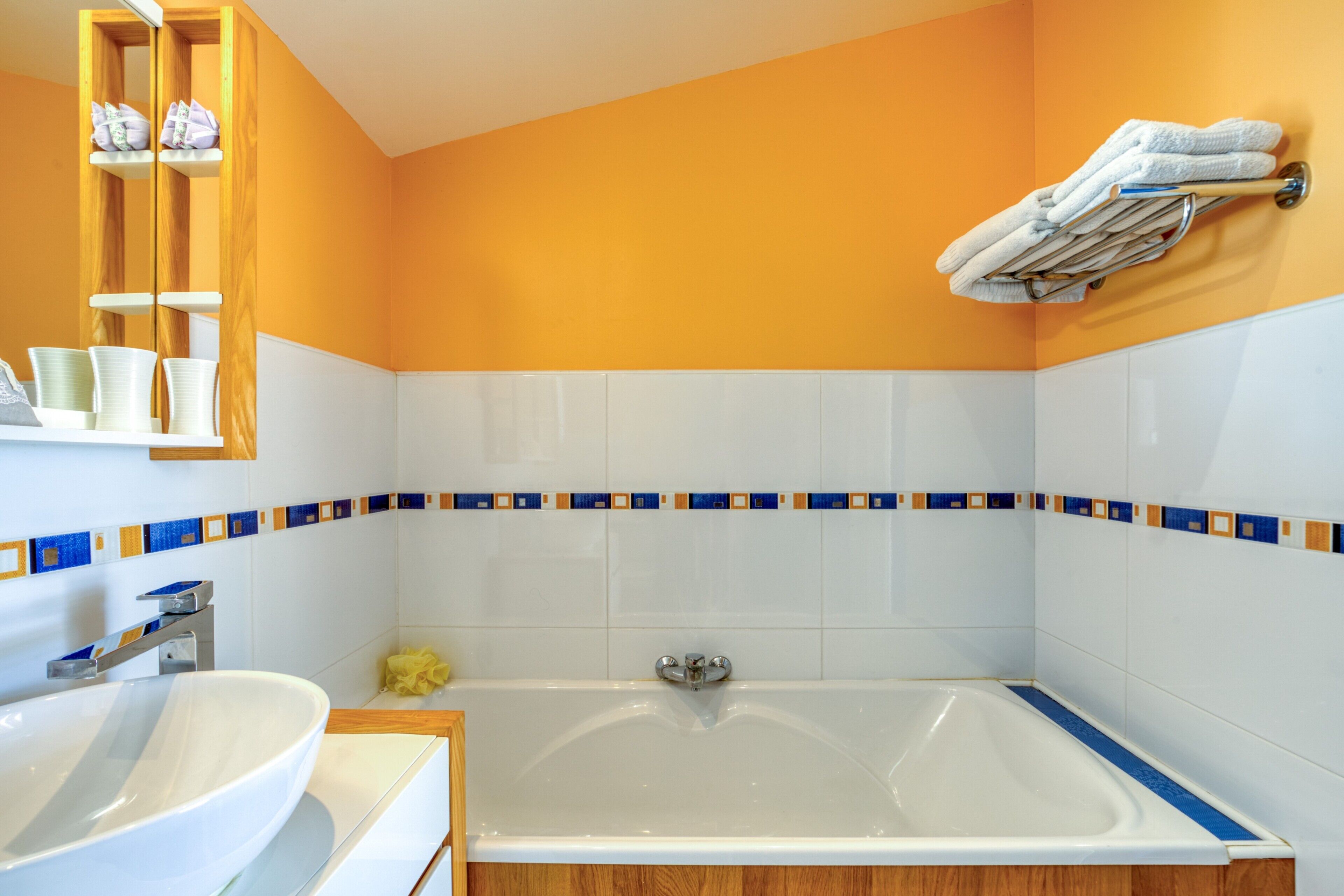 Un baño con bañera, dos lavamanos, un perchero y un estante con artículos de aseo.