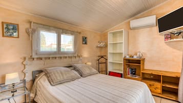 A bedroom with a bed, a bedside table, a window with curtains, a wall-mounted TV, and a shelf with books.