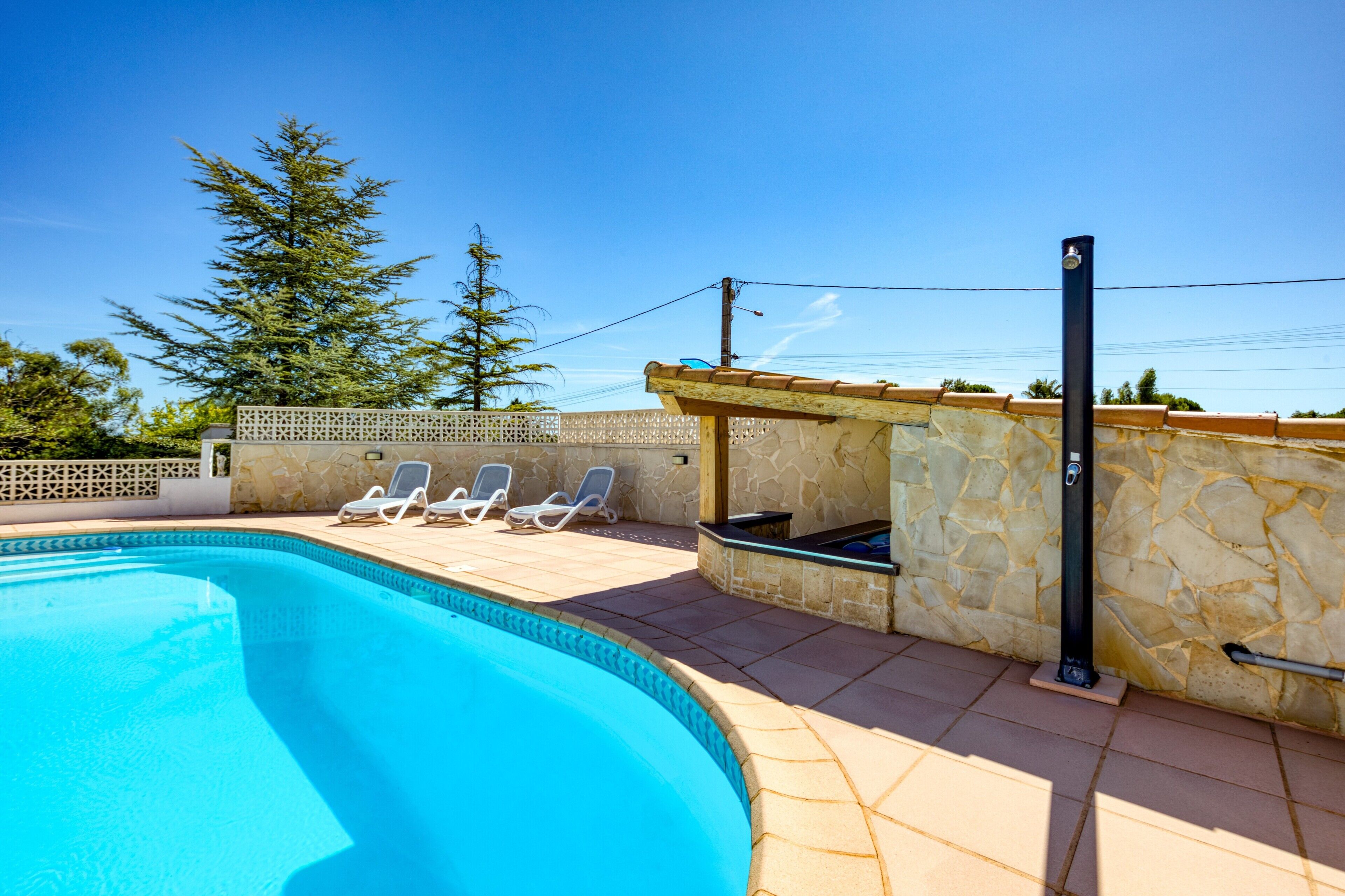 Una piscina con lettini, un muro in pietra e un pergolato.