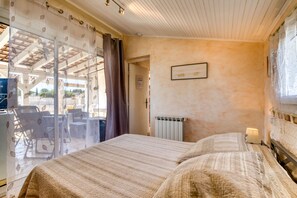 Une chambre à coucher avec un lit, un radiateur, un tableau accroché au mur et une vue par la fenêtre, qui est ornée de rideaux.