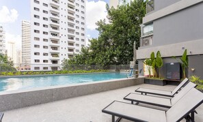 A rooftop pool area with lounge chairs, a pool, and a view of high-rise buildings.