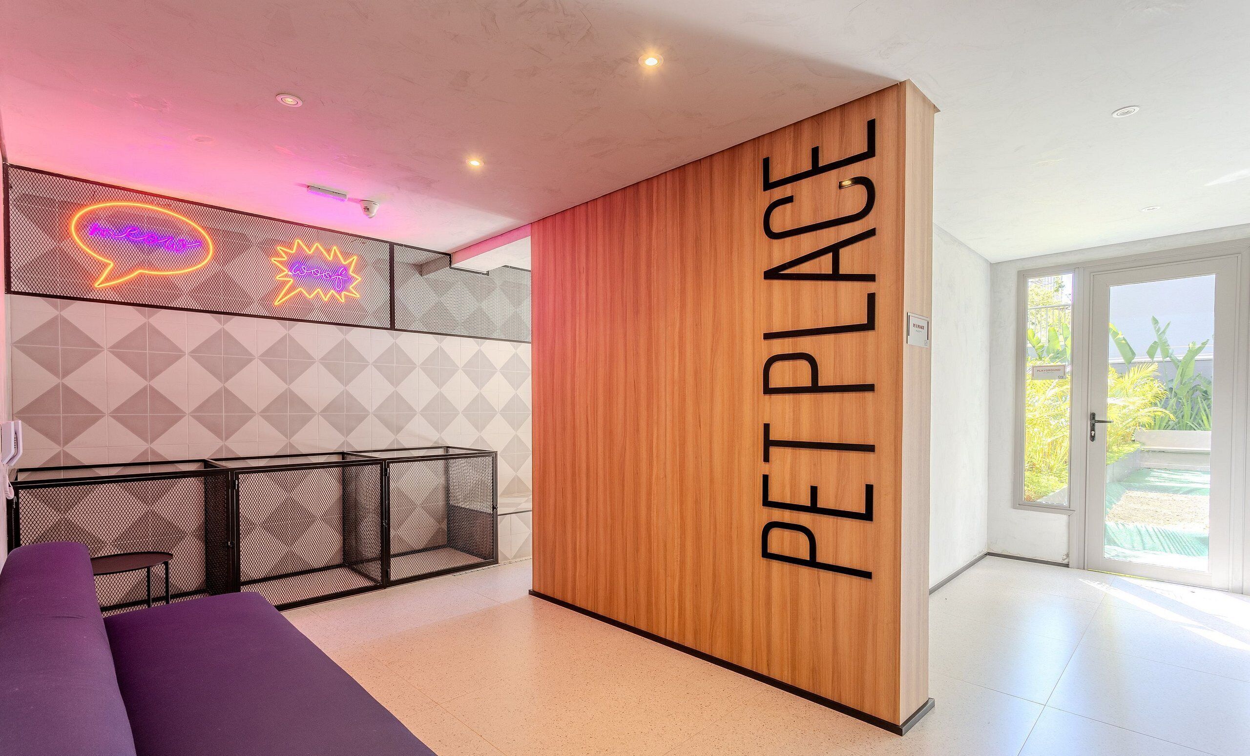 A pet-friendly area with a wooden partition labeled "PET PLACE," a neon sign, a geometric wall pattern, and a seating area with a purple couch.