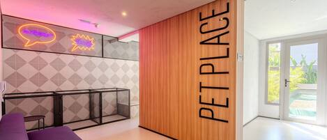 A pet-friendly area with a wooden partition labeled "PET PLACE," a neon sign, a geometric wall pattern, and a seating area with a purple couch.