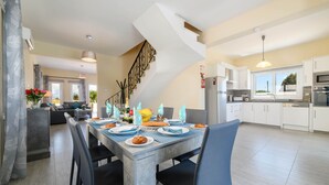 A modern kitchen with white cabinets, a built-in oven, and a dining area with a grey table set for four.