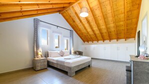 A bedroom with a sloped ceiling, a bed, a nightstand, a chair, and a small desk area.
