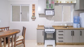 Une cuisine compacte équipée d’une cuisinière à gaz, d’un four, d’un four à micro-ondes et d’un distributeur d’eau. On y trouve une table à manger avec des chaises et une décoration murale.