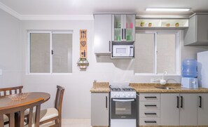 Une cuisine compacte équipée d’une cuisinière à gaz, d’un four, d’un four à micro-ondes et d’un distributeur d’eau. On y trouve une table à manger avec des chaises et une décoration murale.