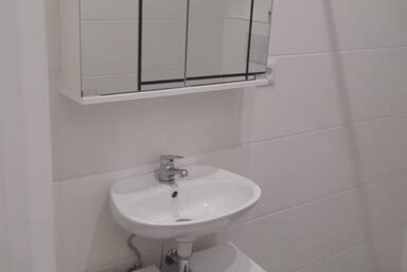 Un baño con un lavabo blanco, un espejo y una pared de azulejos blancos.