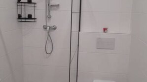 A bathroom with a shower, toilet, and a small shelf with toiletries.