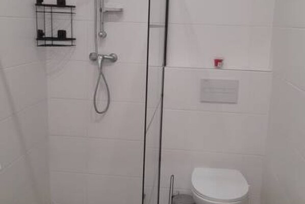 A bathroom with a shower, toilet, and a small shelf with toiletries. - Urban Chic 1BR in Vienna’s Heart (Vienna)