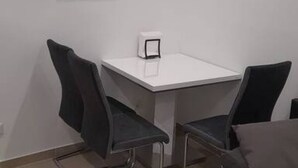 A small, white table with two black chairs, a framed picture on the wall, and a white object on the table.