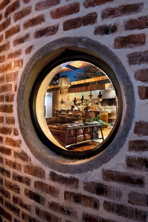 A circular window with a view of a cozy interior featuring a leather sofa, wooden tables, and hanging lights. - Dzombo Camp (Pilanesberg National Park)