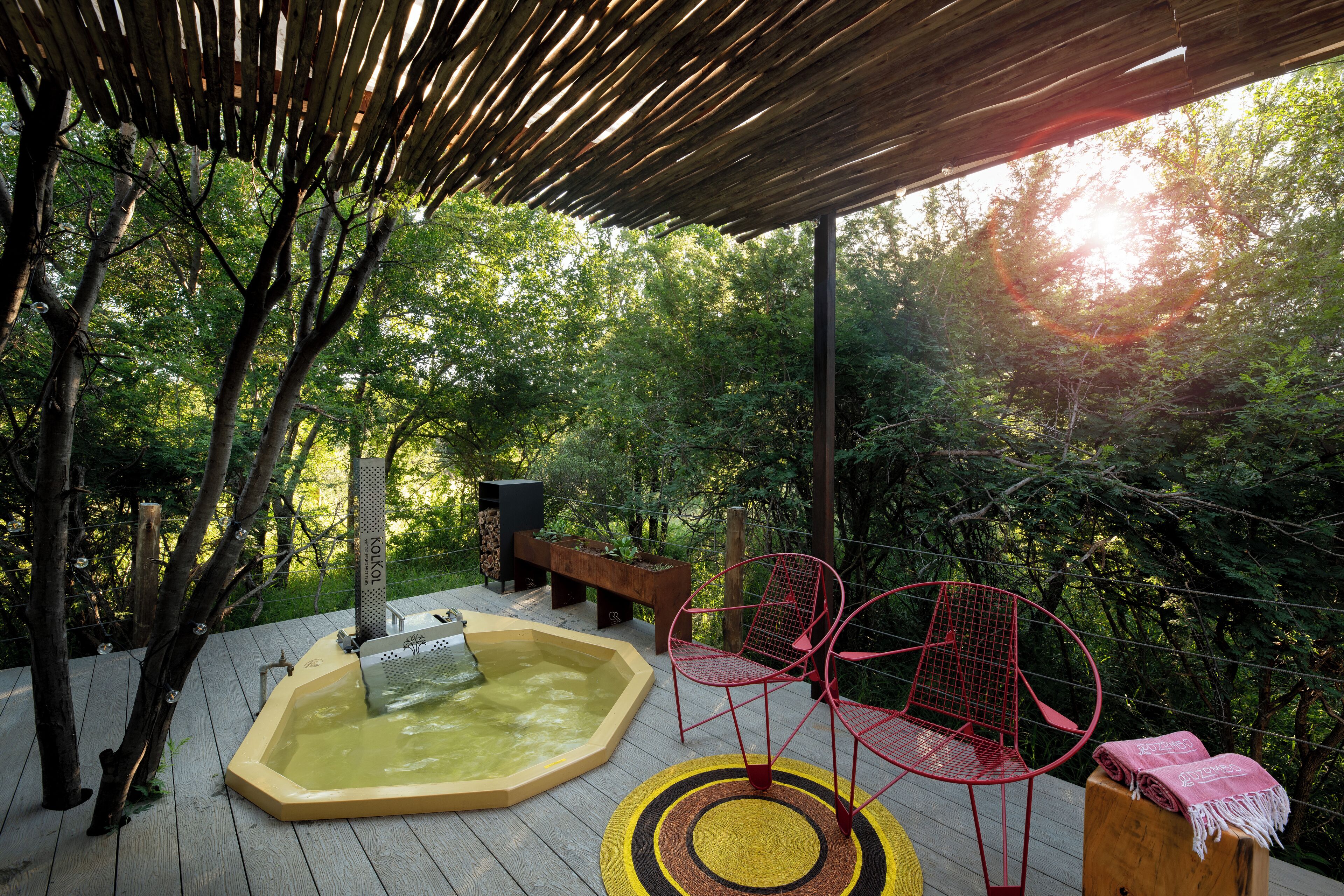Una terraza de madera con un jacuzzi, sillas rojas y una pérgola.