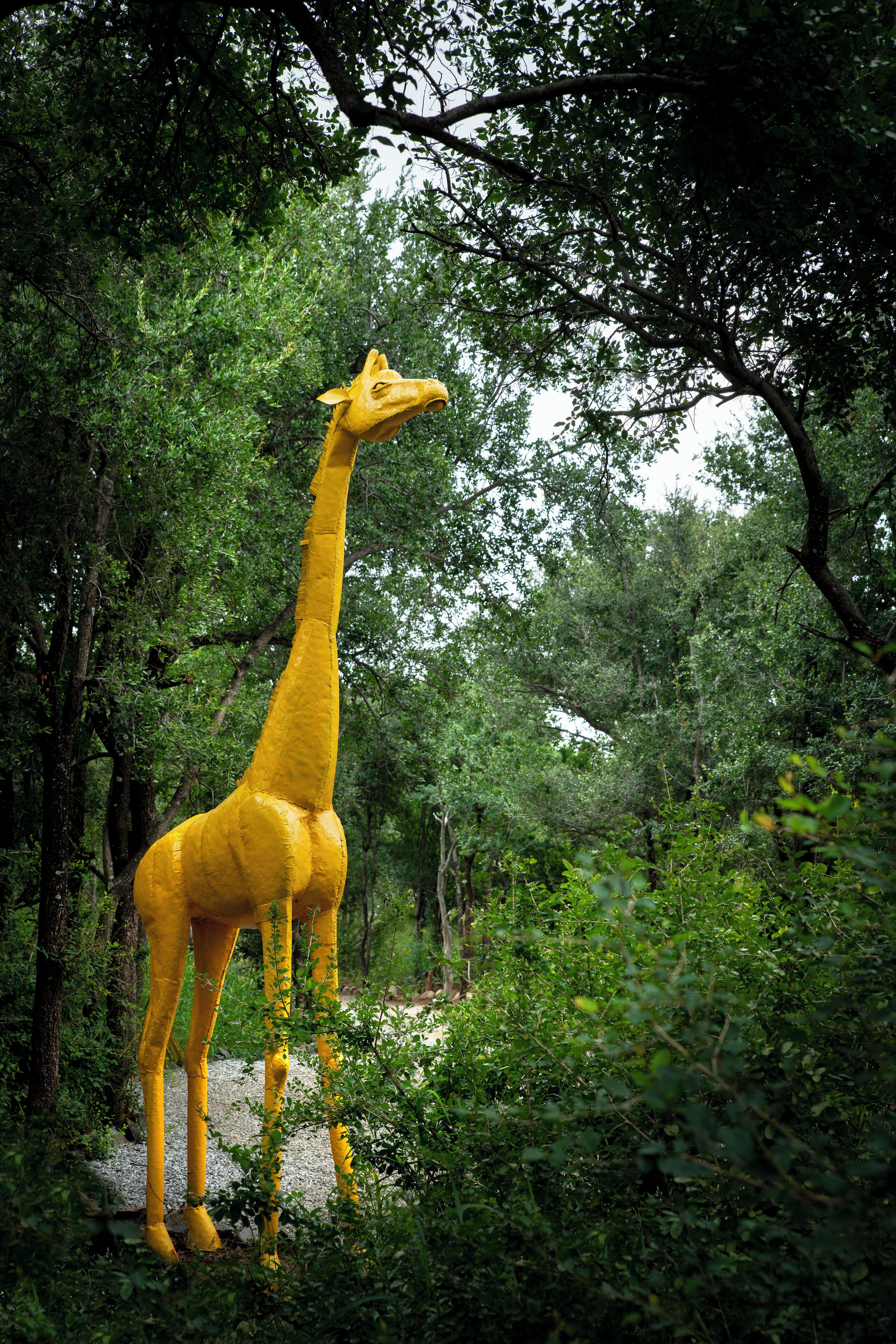 A large yellow giraffe statue in a forested area.