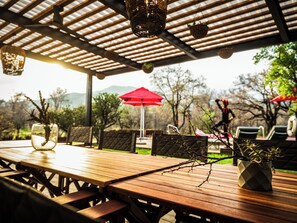 An outdoor patio with wooden tables and chairs, a red umbrella, and hanging lanterns. - Dzombo Camp (Pilanesberg National Park)