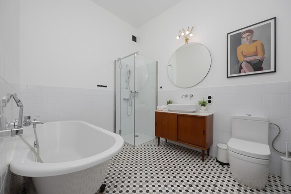 A modern bathroom with a freestanding bathtub, a glass-enclosed shower, a wooden vanity, and a toilet.