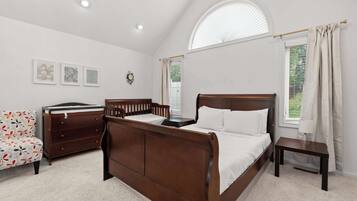 A bedroom with a wooden bed, a dresser, a chair, and a small table. There are three framed pictures on the wall and a window with curtains.