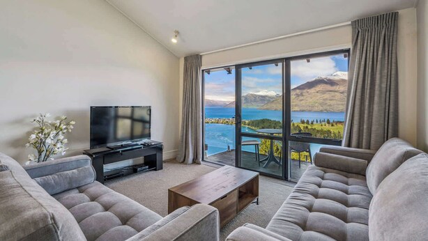 A modern living room with a large window offering a scenic view of a lake and mountains. - Outlook Oasis, Uninterrupted Lake Views (Queenstown)
