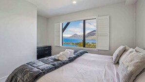 A bedroom with a bed, a dresser, and a window with a scenic view. - Outlook Oasis, Uninterrupted Lake Views (Queenstown)