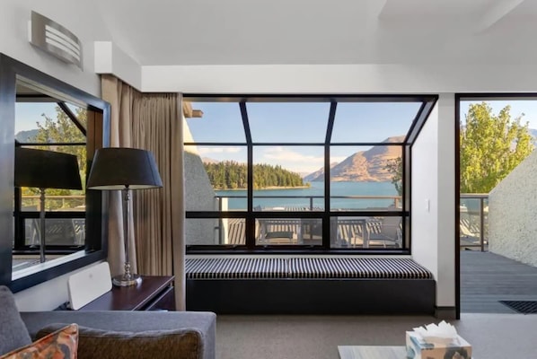 A modern hotel room with a large window offering a scenic view of mountains and a lake.