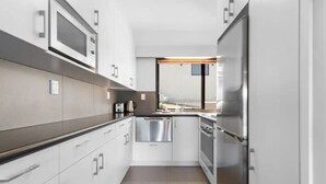 Cocina moderna con armarios blancos, electrodomésticos de acero inoxidable y un ventanal que proporciona luz natural.