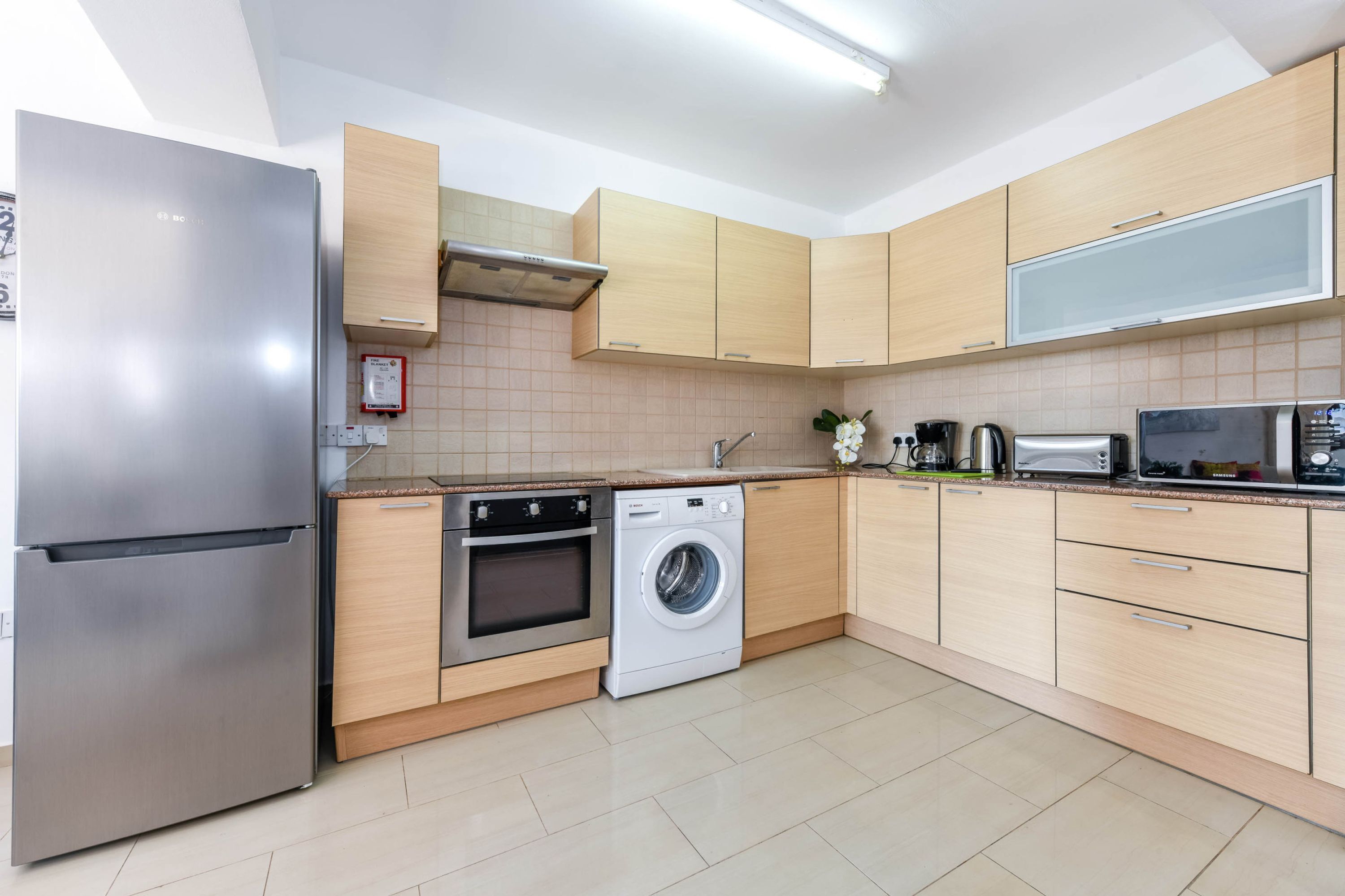 A modern kitchen with stainless steel appliances, wooden cabinets, a built-in oven, and a washing machine.