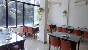 Un salón de conferencias con ventanas amplias, paredes blancas y varias mesas con sillas.