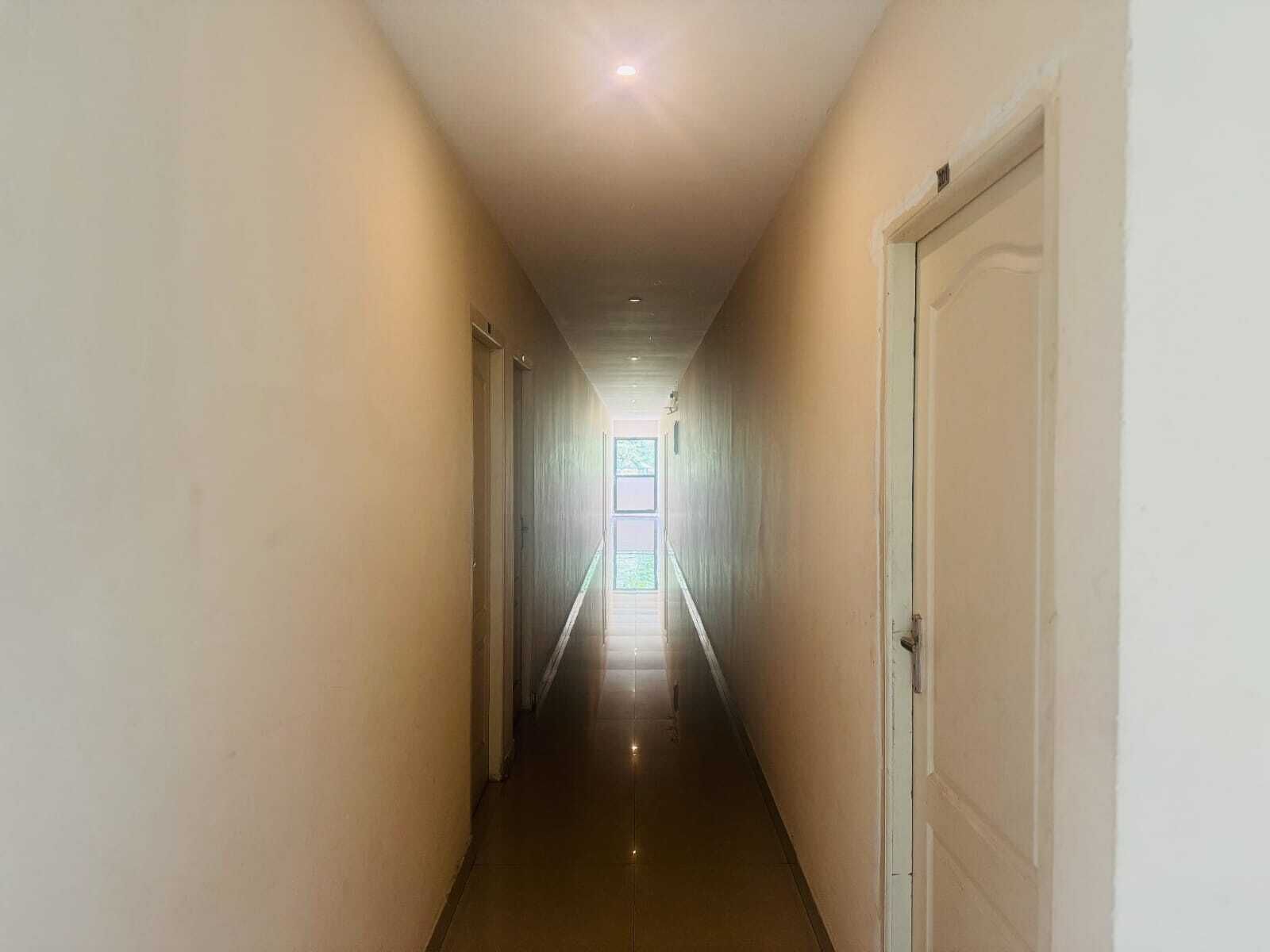 Un pasillo estrecho, bien iluminado, con paredes blancas y suelo de baldosas, que conduce a una puerta al final.