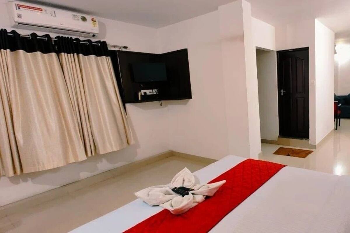 Quarto de hotel com cama, televisão de tela plana, garrafa de água e porta que dá para outro quarto.