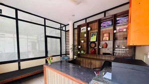 Un área de recepción con un mostrador de madera, un ventanal con persianas y un panel de pared con diversos objetos.