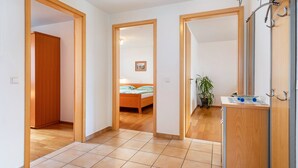 A hallway leading to a bedroom with a bed, a bathroom with a mirror and sink, and a potted plant.