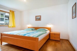 A bedroom with a wooden bed, bedside tables, a window with yellow curtains, and a framed picture on the wall.