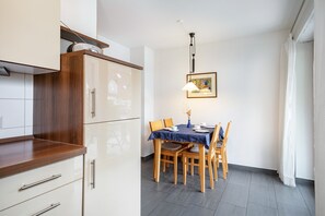 A modern kitchen with wooden cabinets, a dining table with chairs, and a pendant light.