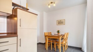 Eine kleine Küche mit Essbereich, Holzschränken, Fliesenboden und einem gerahmten Bild an der Wand.