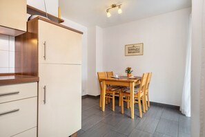 A compact kitchen with a dining area, wooden cabinets, a tiled floor, and a framed picture on the wall.