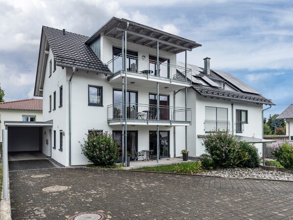 A two-story residential building with a garage, a balcony, and a small patio area.