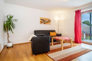 A living room with a sofa, a small table, a lamp, a potted plant, and a painting on the wall.