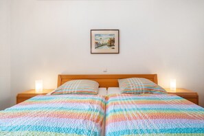 A double bed with a colorful striped bedspread, two bedside lamps, and a framed picture on the wall.