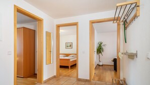 Ein Flur mit einem hölzernen Kleiderschrank, einem Bett mit Holzgestell, einer Zimmerpflanze und einem an der Wand befestigten Wäscheständer.