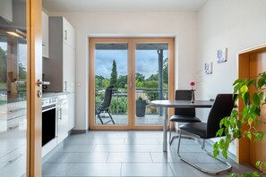 Une cuisine moderne avec un coin repas, une porte-fenêtre coulissante donnant sur un balcon et une plante en pot.