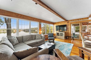 A cozy cabin with a large sofa, a television, and a dining area with a view of a lake.