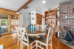A dining area with a round wooden table, white chairs, and a brick fireplace.
