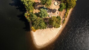 An aerial view of a secluded island with a circular clearing, a small building, and a sandy beach. - Waterfront Retreat | Dock, Kayak & Lake Views (Hopkinton)