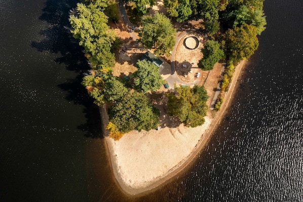 An aerial view of a secluded island with a circular clearing, a small building, and a sandy beach.