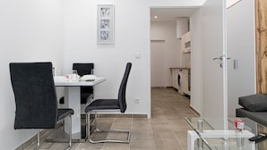 Une pièce moderne comprenant une table à manger, des chaises, une table basse en verre, un canapé et, au fond, un coin cuisine.