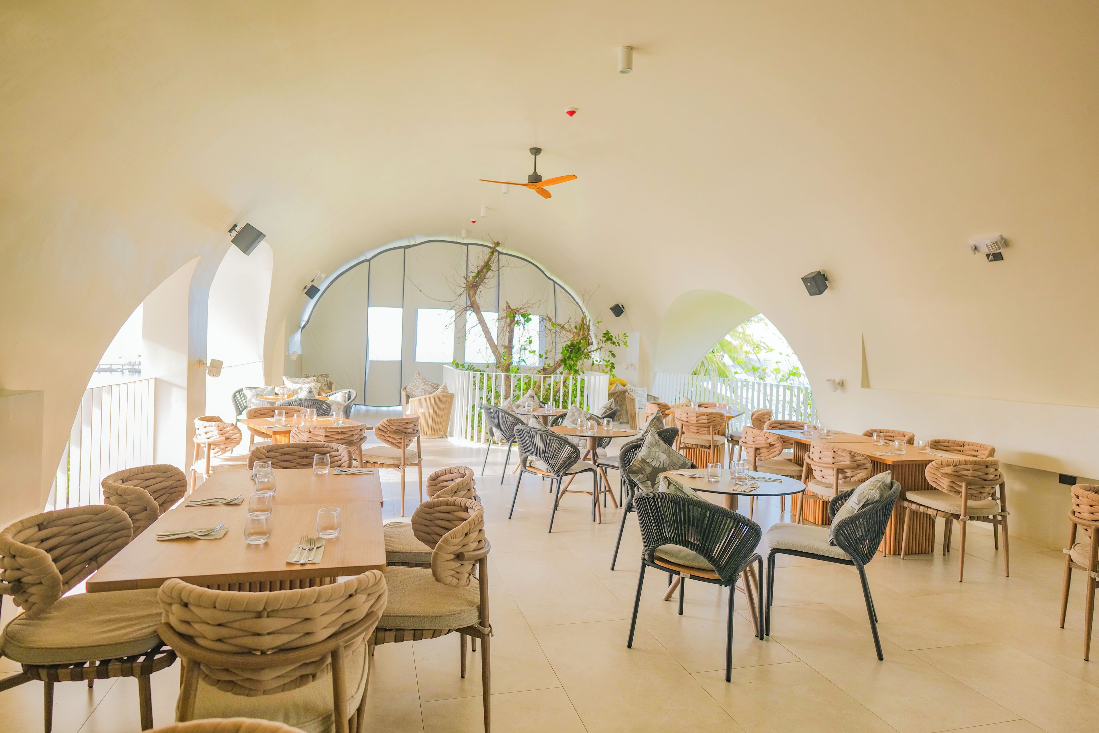 Uma ampla sala de jantar com tetos altos em arco, várias mesas e uma variedade de cadeiras.