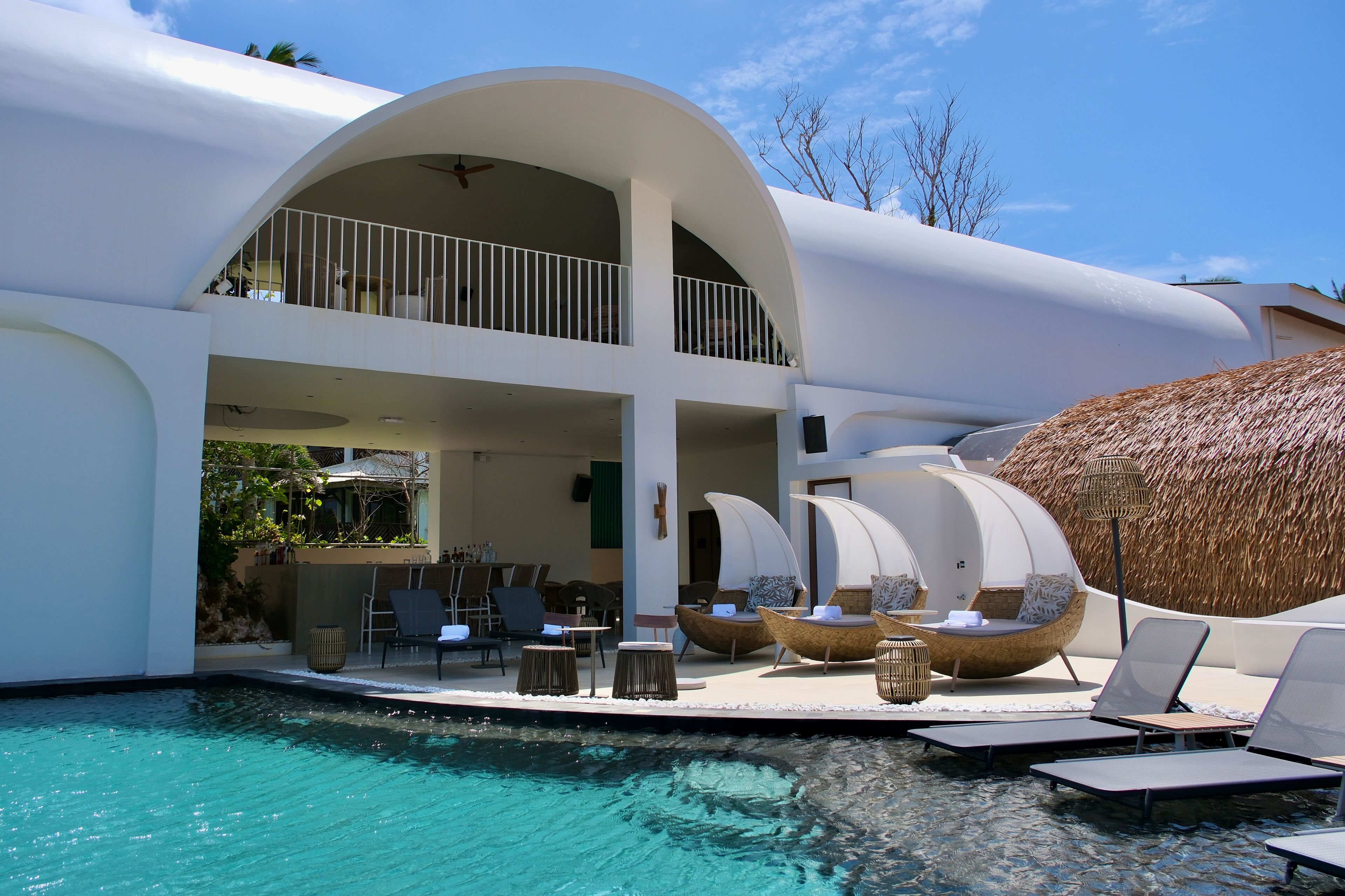 A modern villa with a pool, outdoor seating, and a thatched roof.