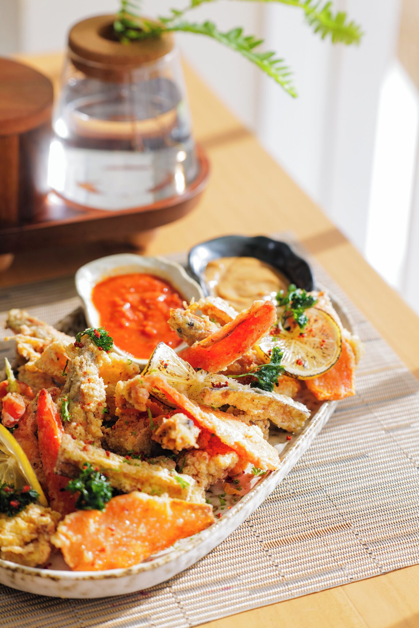 A plate of seafood with lemon slices and herbs, accompanied by a small bowl of sauce.